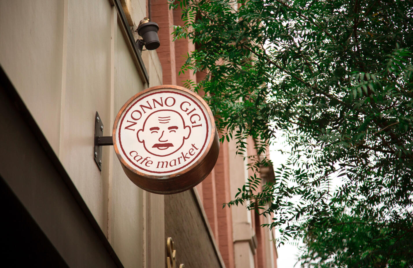 Branding A mockup of a circle storefront sign with a logo of a smiling bald man for Nonno Gigi Cafe Market.